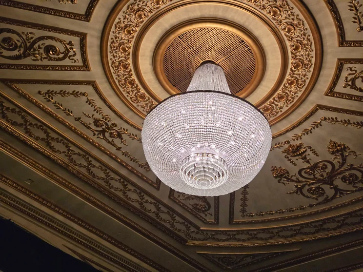 A glass chandelier hanging from an elaborate ceiling