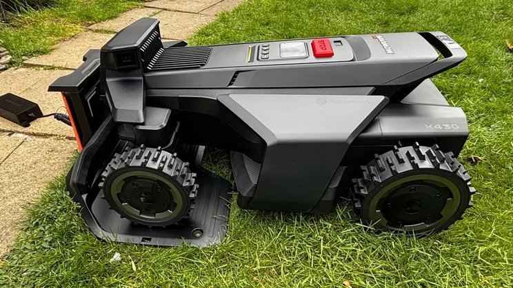 A side view of the Segway Navimow X430 robot lawnmower, docked on its base on a lawn