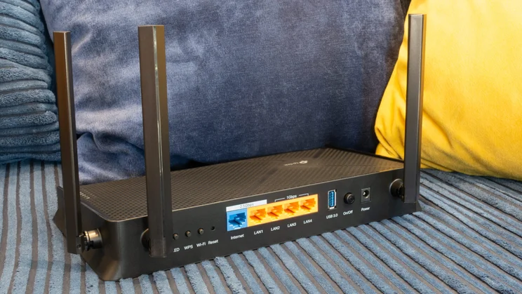 The TP Link Archer BE3600 pictured from the rear in front of a pair of colourful cushions