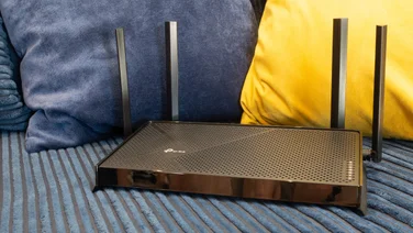 THe TP Link Archer BE3600 pictured in front of two colourful cushions