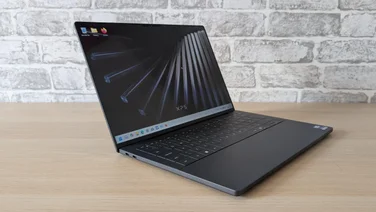 The new Dell XPS 14 laptop on a wooden table with its lid open and screen turned on