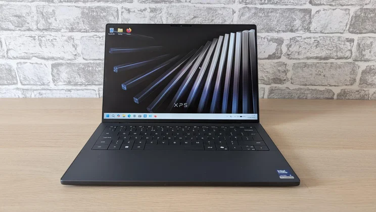 Front view of the new Dell XPS 14 laptop on a wooden table with its lid open and screen turned on