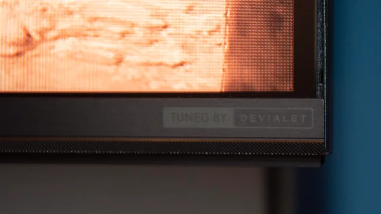 Close-up of the Tuned by Devialet logo on the bottom-right corner of the Hisense UR8S RGB Mini LED TV