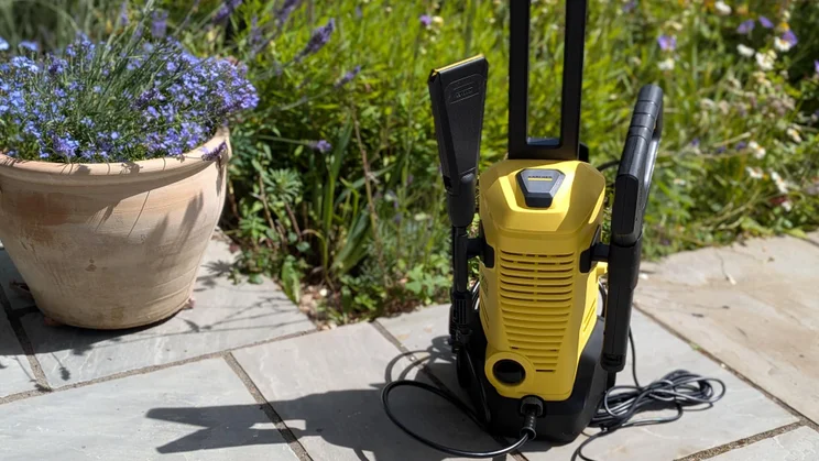 Front view of the K&auml;rcher K3 eco!Booster pressure washer on a patio in front of plants and flowers
