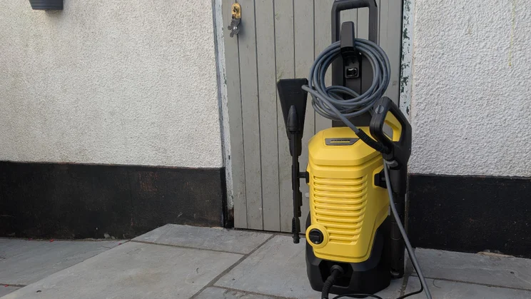 The K&auml;rcher K4 WCM Flex eco!Booster pressure washer in front of an outhouse door