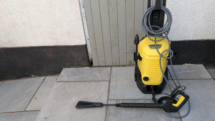 The K&auml;rcher K4 WCM Flex eco!Booster pressure washer with its flat-jet hose attached in front of a door on a patio