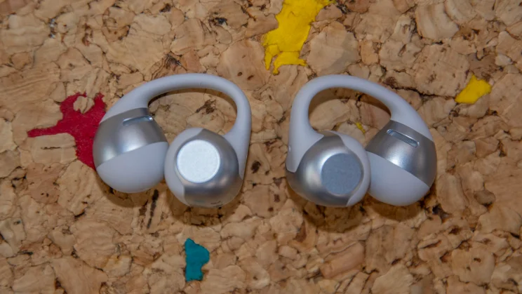 The Shokz OpenDots 2 wireless earbuds lying flat on a cork table