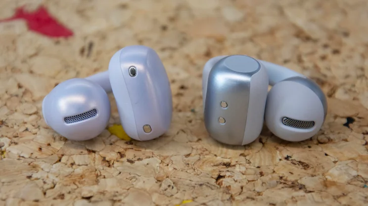 One of the Shokz OpenDots Air wireless earbuds next to a Shokz OpenDots 2 earbud on a cork table