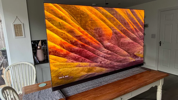 Left view of the TCL X11L SQD Mini LED TV displaying a yellow and reddish landscape screensaver