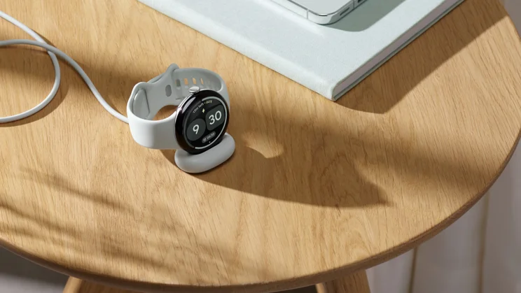 The Pixel Watch 5 on its charging plate, pictured on a wooden side table
