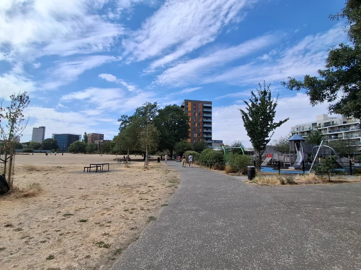 A park with a playground and a large field, buildings in the distance