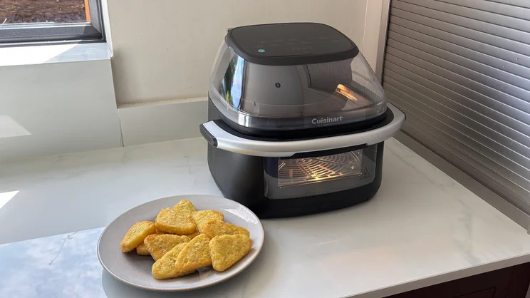The Cuisinart Clearview 9-in-1 air fryer on a kitchen worktop, alongside a plate of cooked hash browns