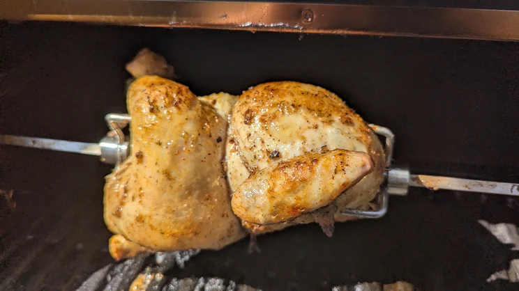 A closeup of a chicken cooking on the Dimplex Crossray eXtreme BBQ's rotisserie attachment