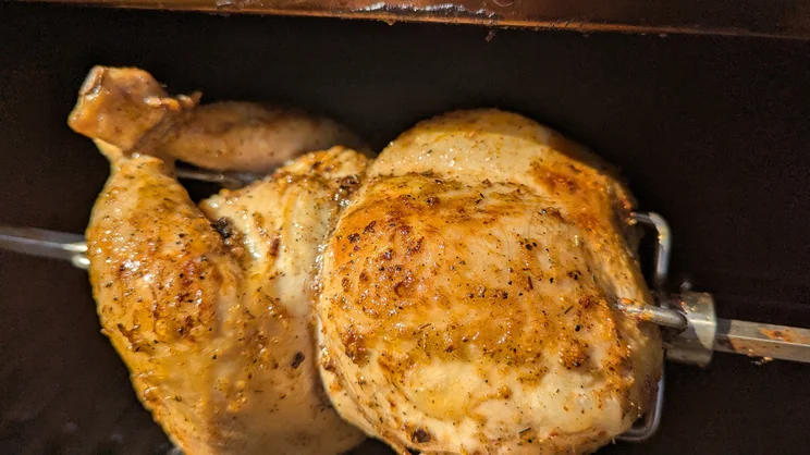 A closeup of a chicken cooking on the Dimplex Crossray eXtreme BBQ's rotisserie attachment