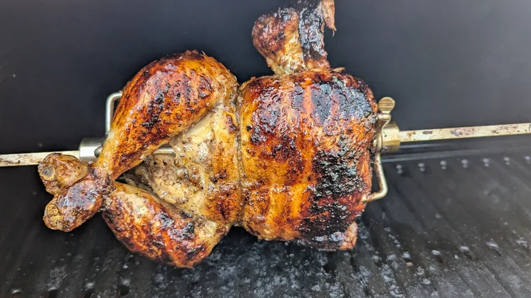 A closeup of a chicken cooking on the Dimplex Crossray eXtreme BBQ's rotisserie attachment