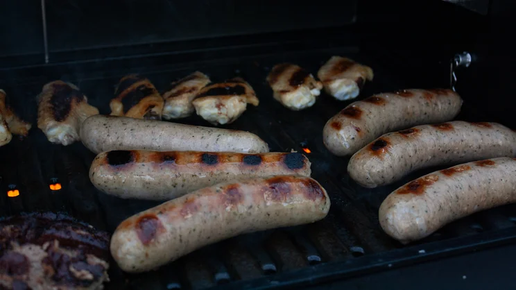 A closeup of sausages cooking on the Dimplex Crossray eXtreme BBQ