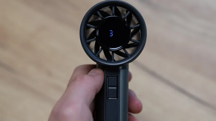 A closeup of the John Lewis High Power Handheld Fan, held in the hand. The fan is turned on and its display is showing the number "3"