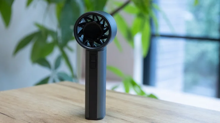 The John Lewis High Power Handheld Fan standing upright on a table in an office