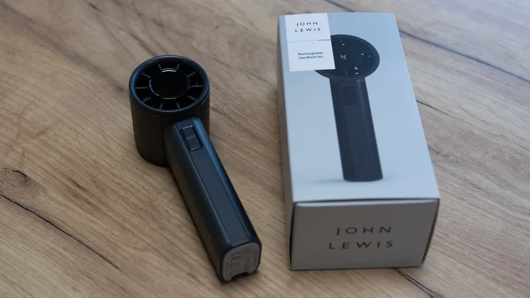 The John Lewis High Power Handheld Fan lying on a table, alongside its box