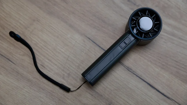 A bird's eye view of the John Lewis High Power Handheld Fan, lying on a table, with its hand strap attached