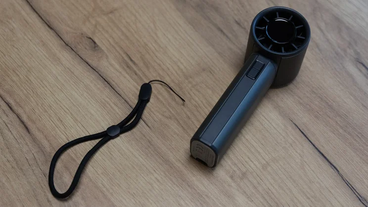 A bird's eye view of the John Lewis High Power Handheld Fan, laid on a table. Its hand strap is detached and lying next to it