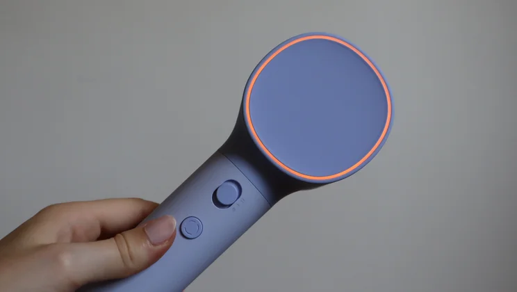 The Laifen Neo hair dryer in a hand, with its LED ring illuminated