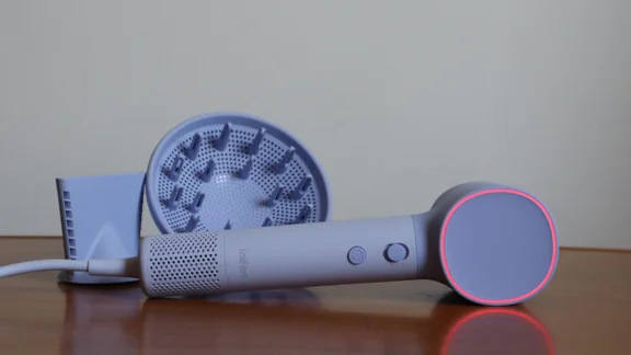 The Laifen Neo hair dryer - with LED ring light illuminated - lying on its side on a table, alongside its attachments