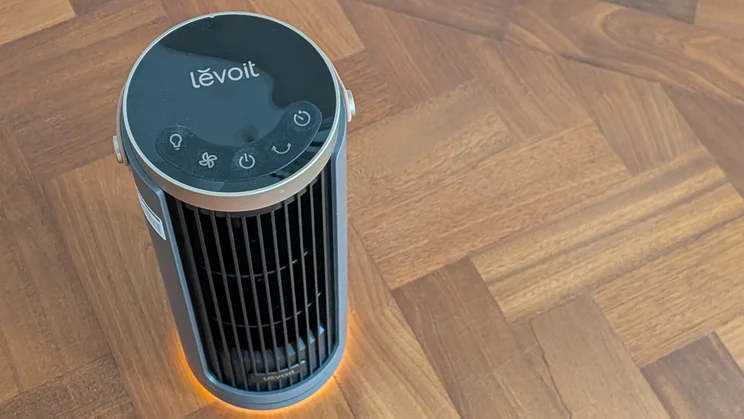 A bird's eye view of the Levoit Windi Mini Pro fan on a parquet floor. Its base ring light is illuminated orange.