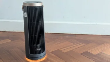The Levoit Windi Mini Pro fan on a parquet in front of a white wall. Its base ring light is illuminated