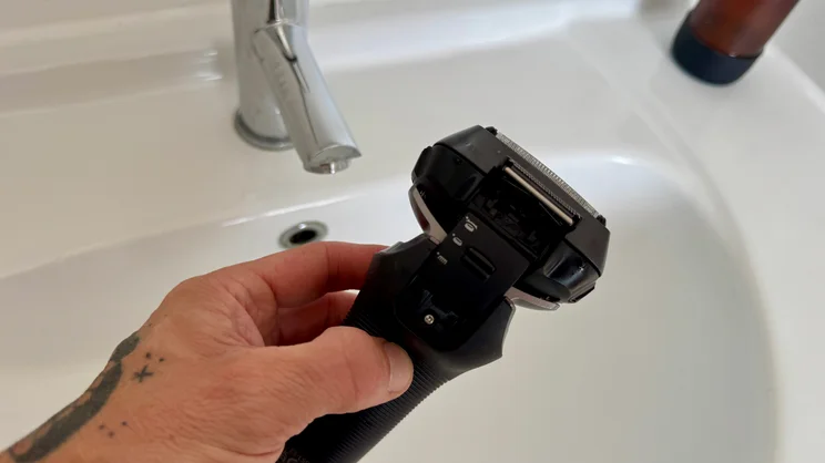The Panasonic Series 900+ electric shaver held over a bathroom sink. Focussed on the shaver's trimmer attachment