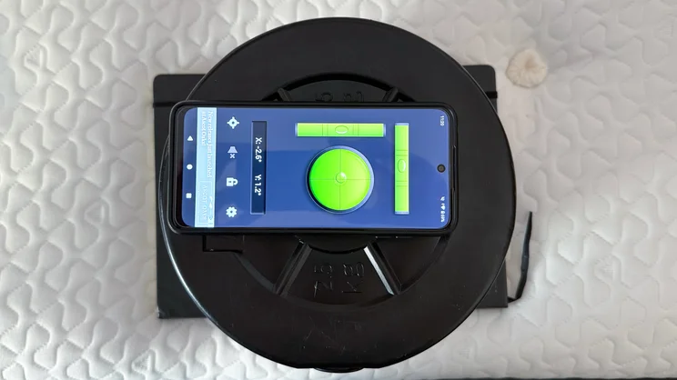 A bird's eye view of a notebook, a series of weights and a smartphone with spirit level app, stacked on top of the Silentnight UltraGel Miracoil Pillowtop mattress' surface