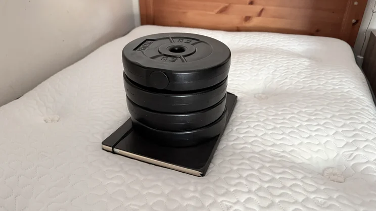 A notebook and a series of weights stacked on top of the surface of the Silentnight UltraGel Miracoil Pillowtop mattress, as per Expert Reviews' mattress deflection tests