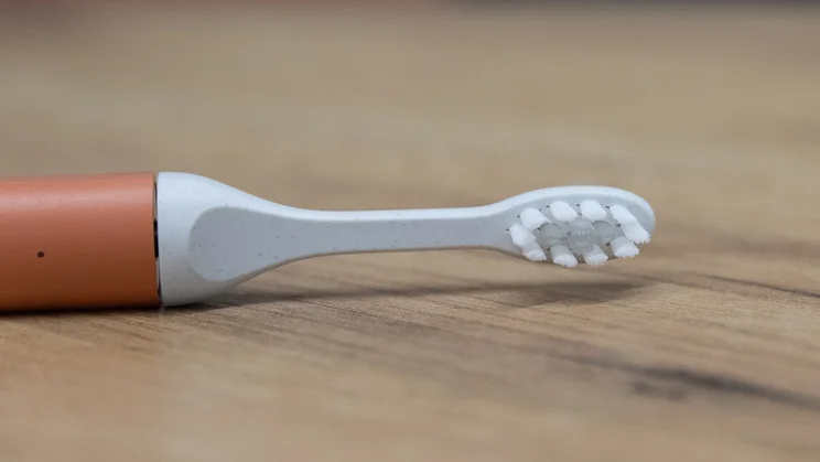 A closeup of the Suri Core 1.0 electric toothbrush, lying on its side on an office table