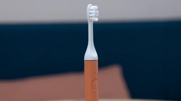 A closeup of the Suri Core 1.0 electric toothbrush, standing upright on an office table