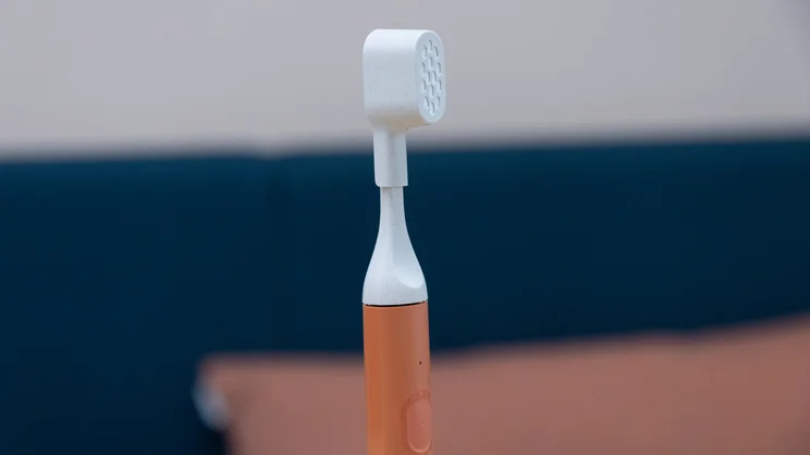 A closeup of the Suri Core 1.0 electric toothbrush, standing upright on an office table. Its travel brush cap is on