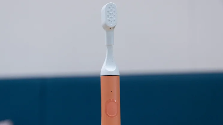 A closeup of the Suri Core 1.0 electric toothbrush, upright on an office table. Its travel brush cap is on
