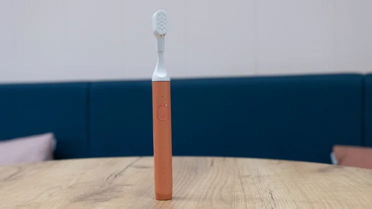 The Suri Core 1.0 electric toothbrush standing upright on a table in an office. Its travel brush cap is on