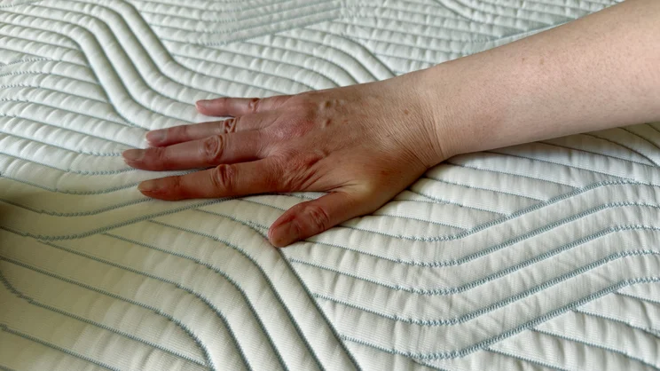 A hand pushing down on the surface of the Tempur Pro Plus SmartCool mattress