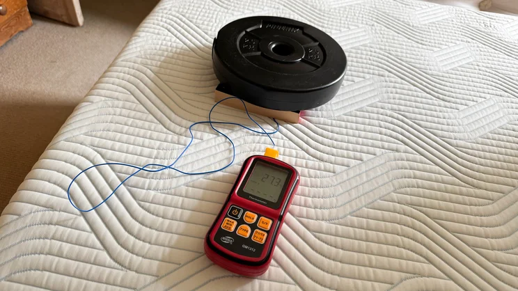 A thermocouple probe, dumbbell plate and book being used to measure temperature retention on the surface of the Tempur Pro Plus SmartCool mattress