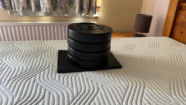 A stack of dumbbell plates and a notebook, being used to measure deflection of the surface of the Tempur Pro Plus SmartCool mattress