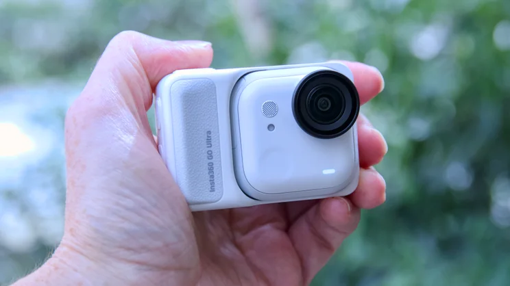 The Insta360 Go Ultra pictured in hand, in its dock
