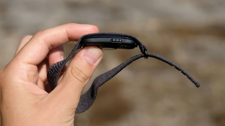 Side view of the Garmin Cirqa tracker attached to its strap being held between thumb and forefinger