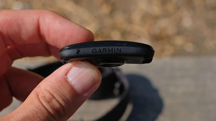 Side view of the Garmin Cirqa tracker being held between a thumb and forefinger