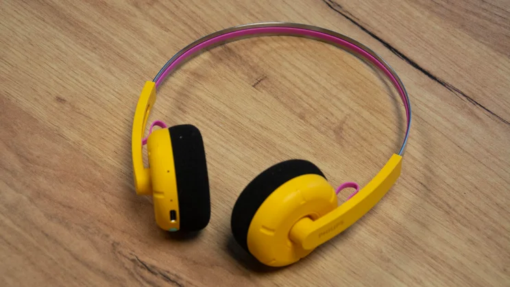 The Philips Ringo Duo on-ear headphones in yellow on a wooden table