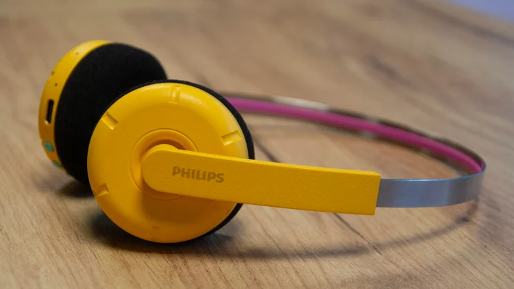 Side view of the Philips Ringo Duo on-ear headphones in yellow on a wooden table