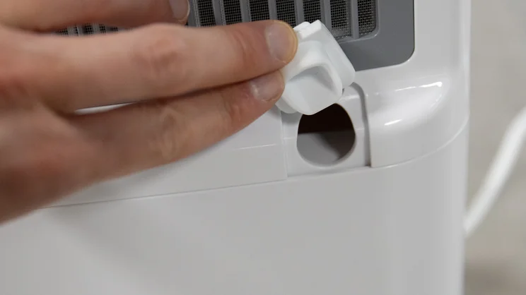 A closeup of the Devola DVH12L Compressor dehumidifier's continuous draining output hole. A hand is holding its cover open