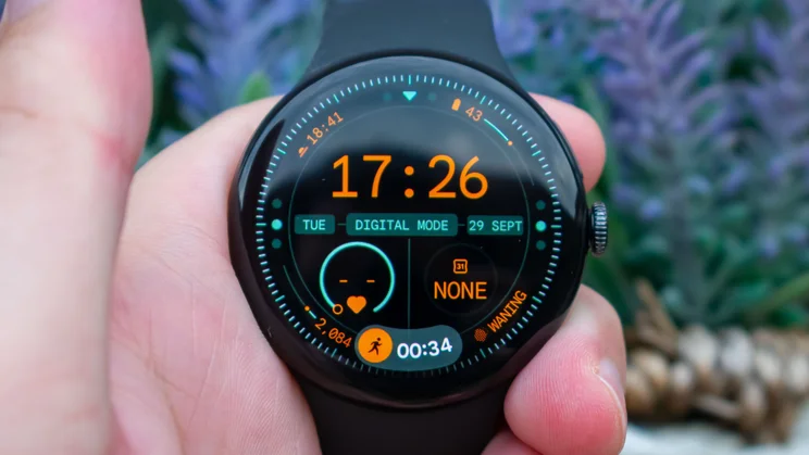 Google Pixel Watch 5 in hand, displaying home page with workout At a Glance widget at the bottom