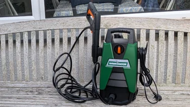 Hawksmoor High Pressure Washer 108 bar upright on a garden bench with the trigger gun stowed on its side holder and the power cable wrapped on the other.