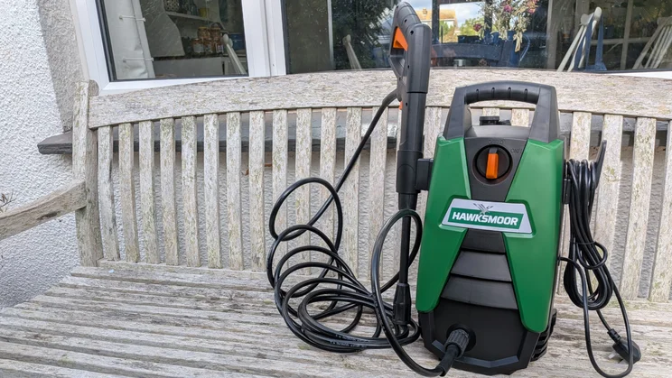 Hawksmoor High Pressure Washer 108 bar on a wooden bench outside patio doors, with the hose looped in front and the trigger gun held in its holder.