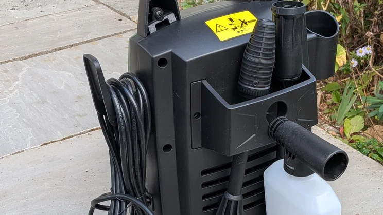 Rear of the Hawksmoor High Pressure Washer 108 bar showing the accessory tray with nozzle attachments, a detergent bottle, a cable hook and a yellow warning label.